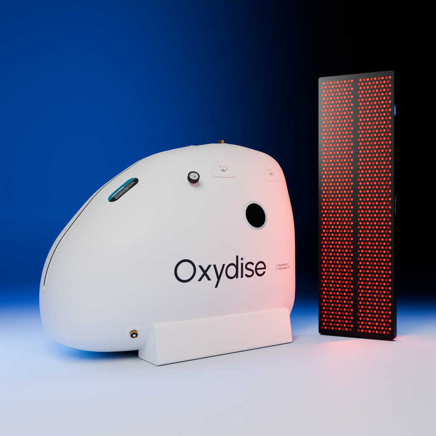 Oxydise sitting Hyperbaric Oxygen chamber (1.5 ATA) beside the Oxydise Red Light Therapy panel, both angled, in the blue studio