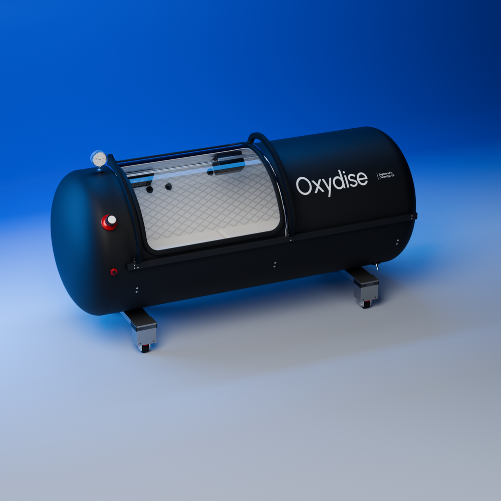 Oxydise lying hardshell chamber in the Blue Studio, showing the curved viewing window and full-width silver leg supports.