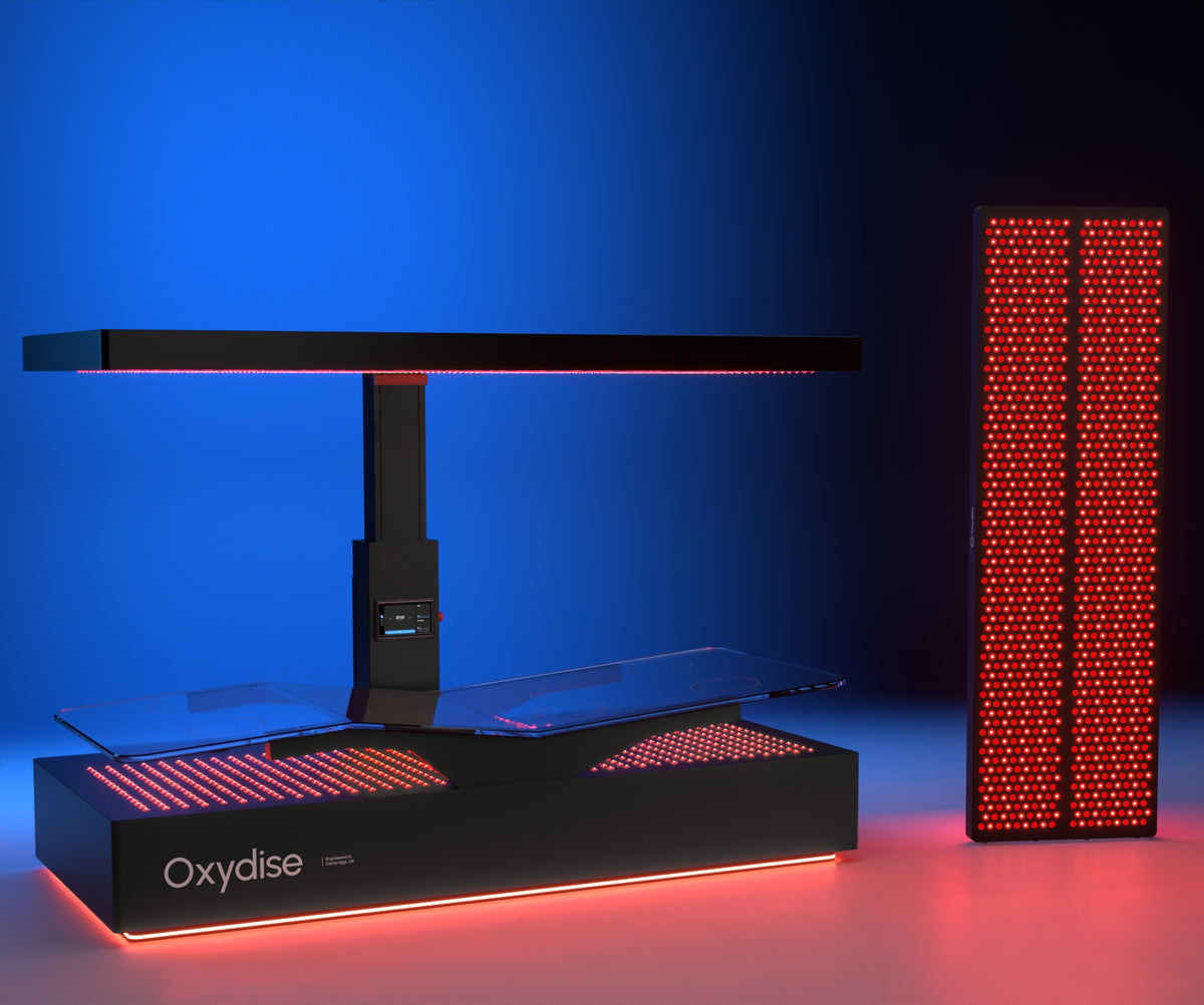 Oxydise Red Light and PEMF bed beside an illuminated Red Light panel, photographed from a lower angle in the blue studio.