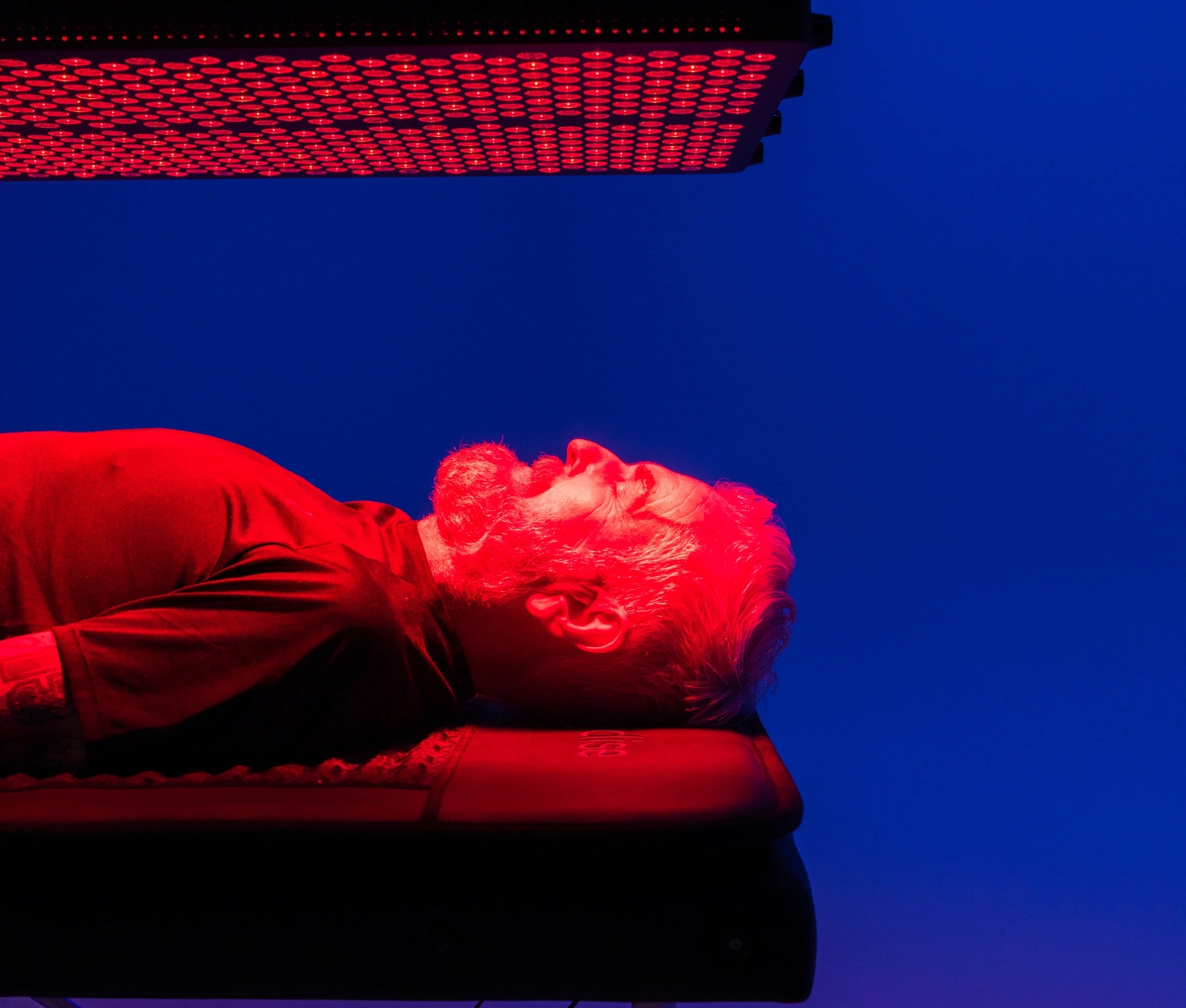 Man receiving Red Light Therapy beneath an illuminated panel in the studio