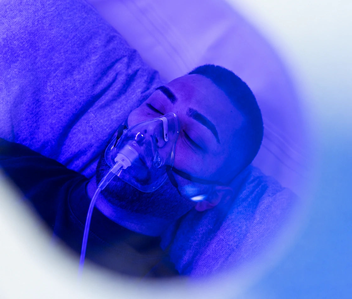 Man lying with his eyes closed inside a Hyperbaric Oxygen chamber, wearing an oxygen mask